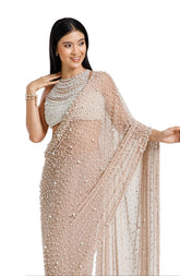 Model wearing a champagne blush net saree hand-embellished with hundreds of cascading white pearls, paired with a matching concentric pearl halter blouse.