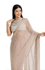 Model wearing a champagne blush net saree hand-embellished with hundreds of cascading white pearls, paired with a matching concentric pearl halter blouse.