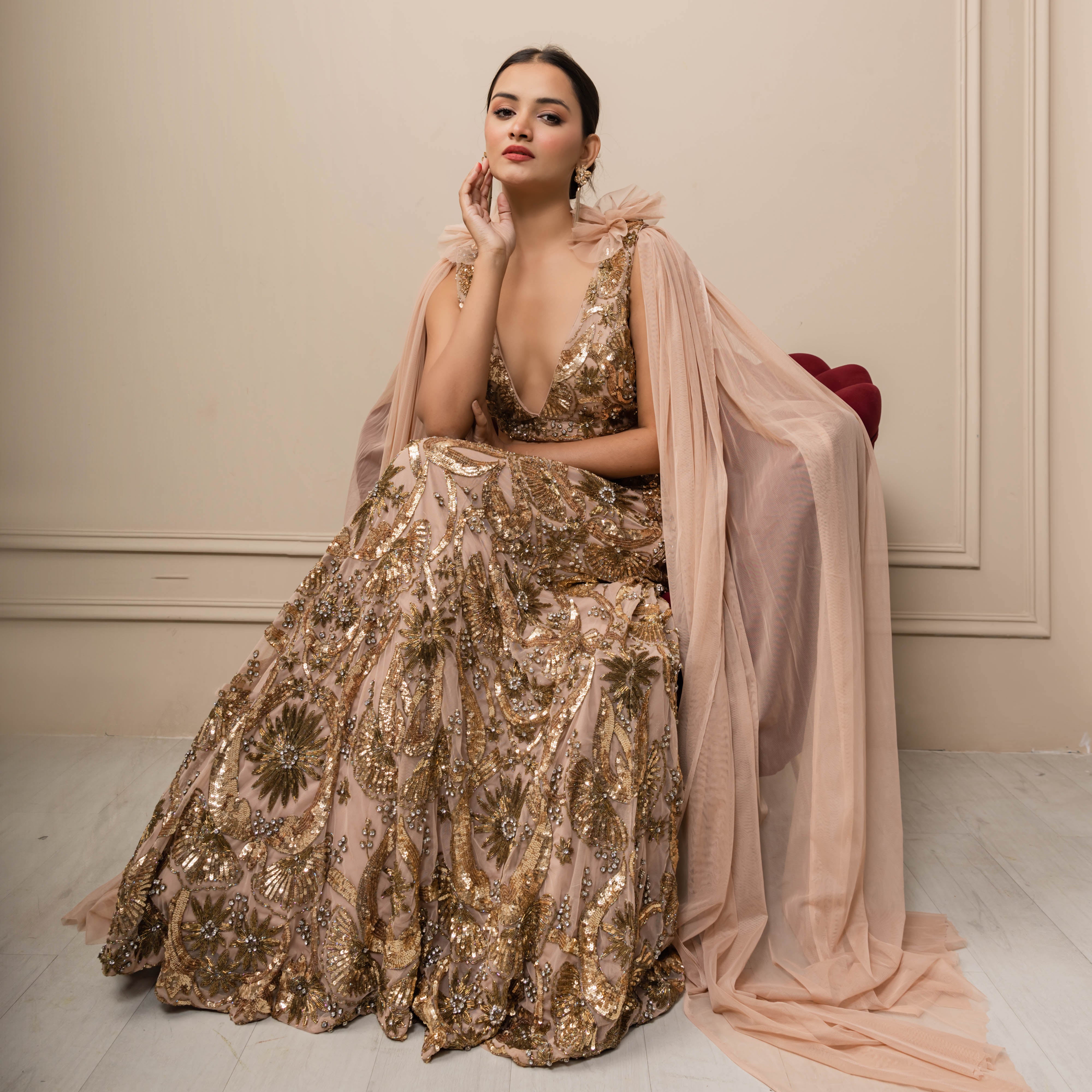 Woman in a gold sequin gown with a pink shawl against a beige wall.