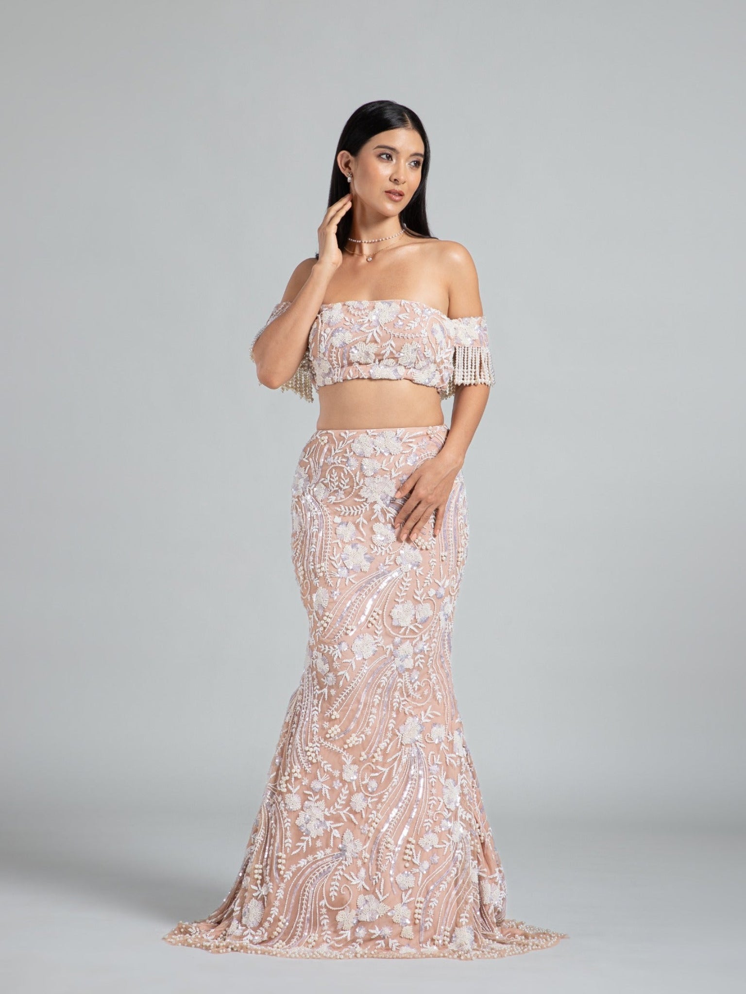 Fish cut beige lehenga by DEEPANSHI MASSEY LABEL featuring intricate floral hand embroidery, an off-shoulder blouse with pearl-fringed sleeves, and a fitted mermaid silhouette.