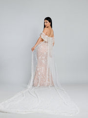 Back view of the beige embroidered fish cut lehenga by DEEPANSHI MASSEY LABEL, featuring a fitted silhouette and a long sheer cape adorned with scattered pearls.