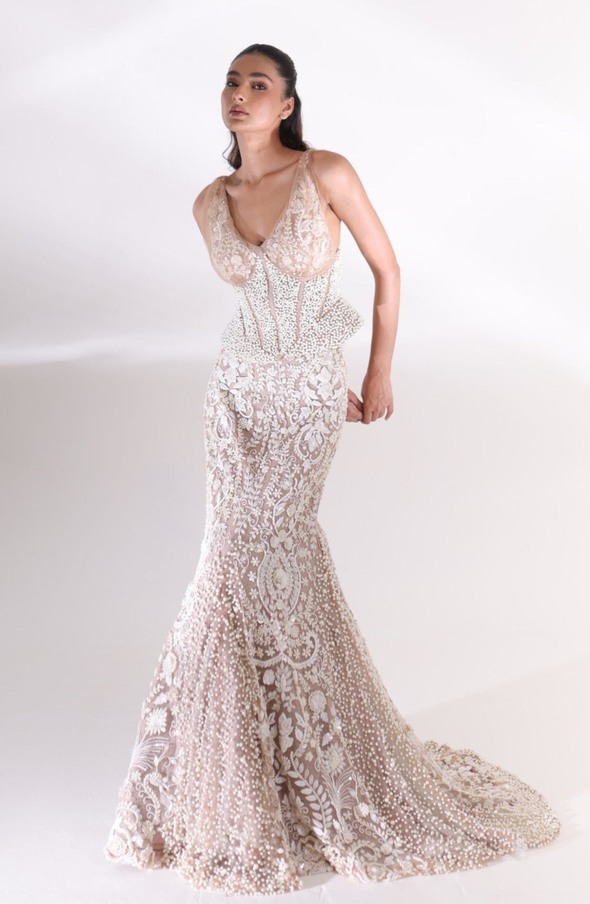 Three-quarter view of the champagne ivory Aurelia Pearl Mermaid Lehenga showcasing intricate floral embroidery, pearl embellishments, a fitted silhouette and an elegant bridal train by DEEPANSHI MASSEY LABEL.