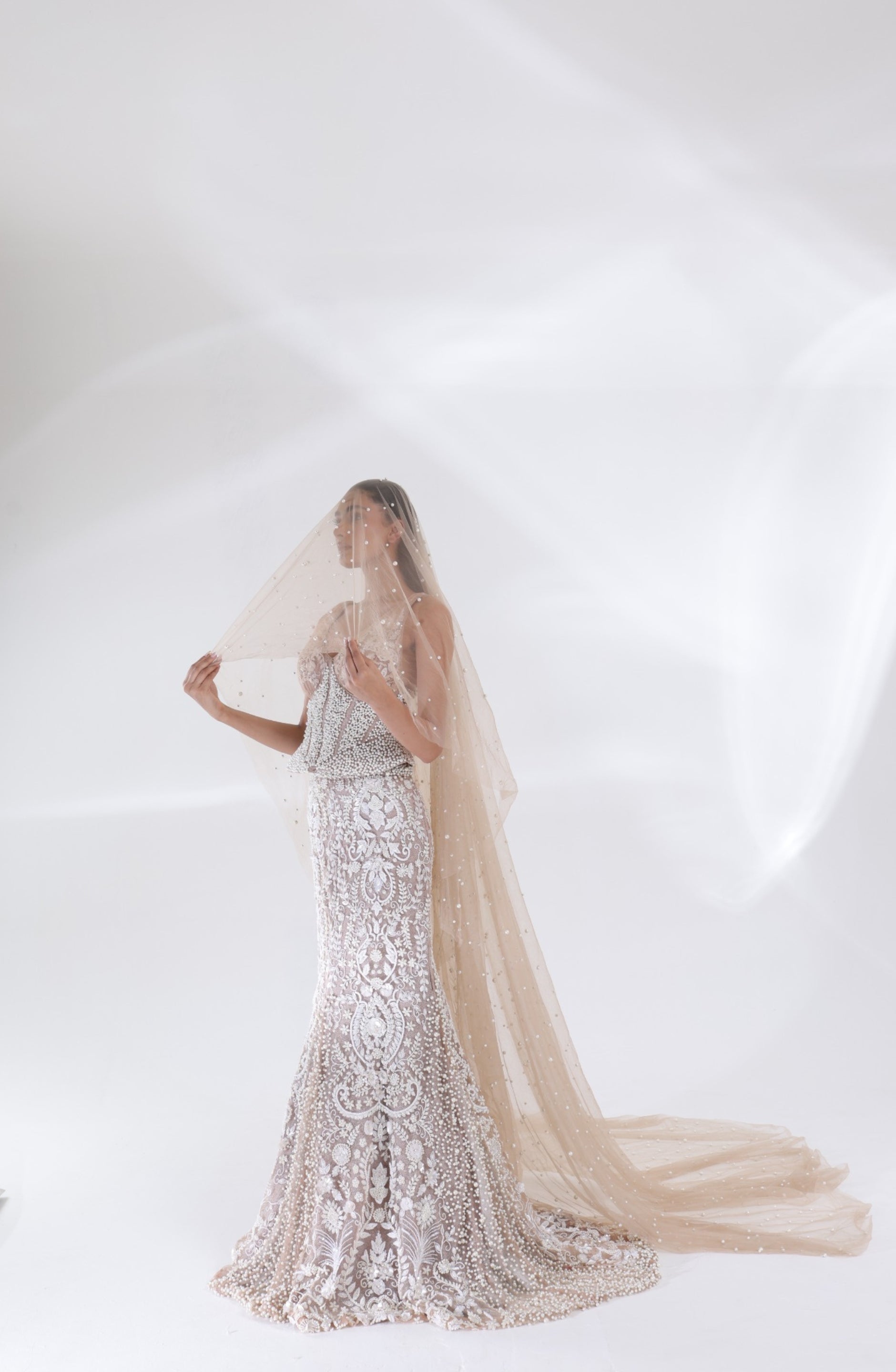 Full-length view of the champagne ivory Aurelia Pearl Mermaid Lehenga showcasing elaborate floral embroidery, a fitted mermaid skirt and pearl detailing along the hem by DEEPANSHI MASSEY LABEL.