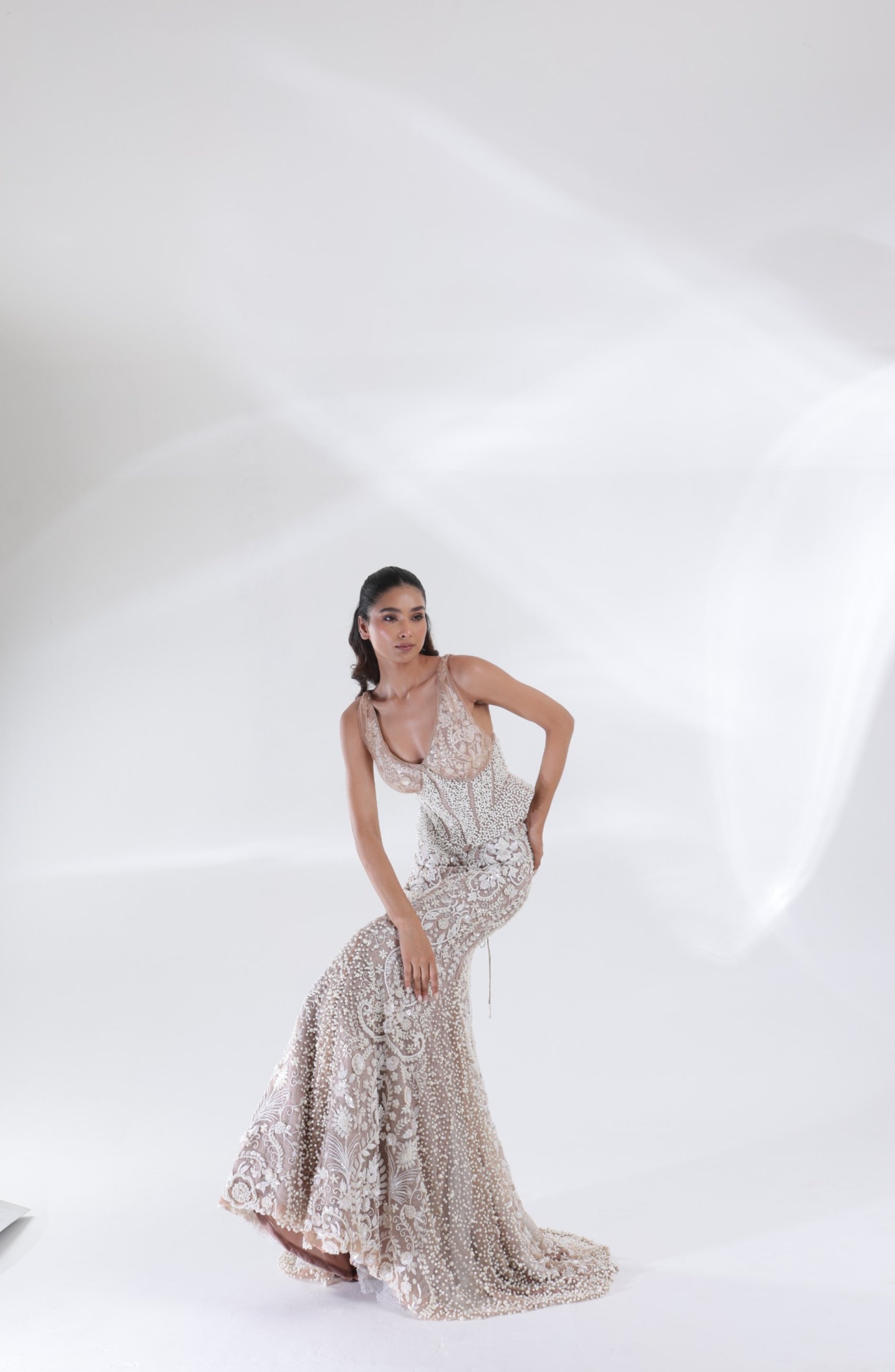 Full-length view of the champagne ivory Aurelia Pearl Mermaid Lehenga showcasing elaborate floral embroidery, a fitted mermaid skirt and pearl detailing along the hem by DEEPANSHI MASSEY LABEL.
