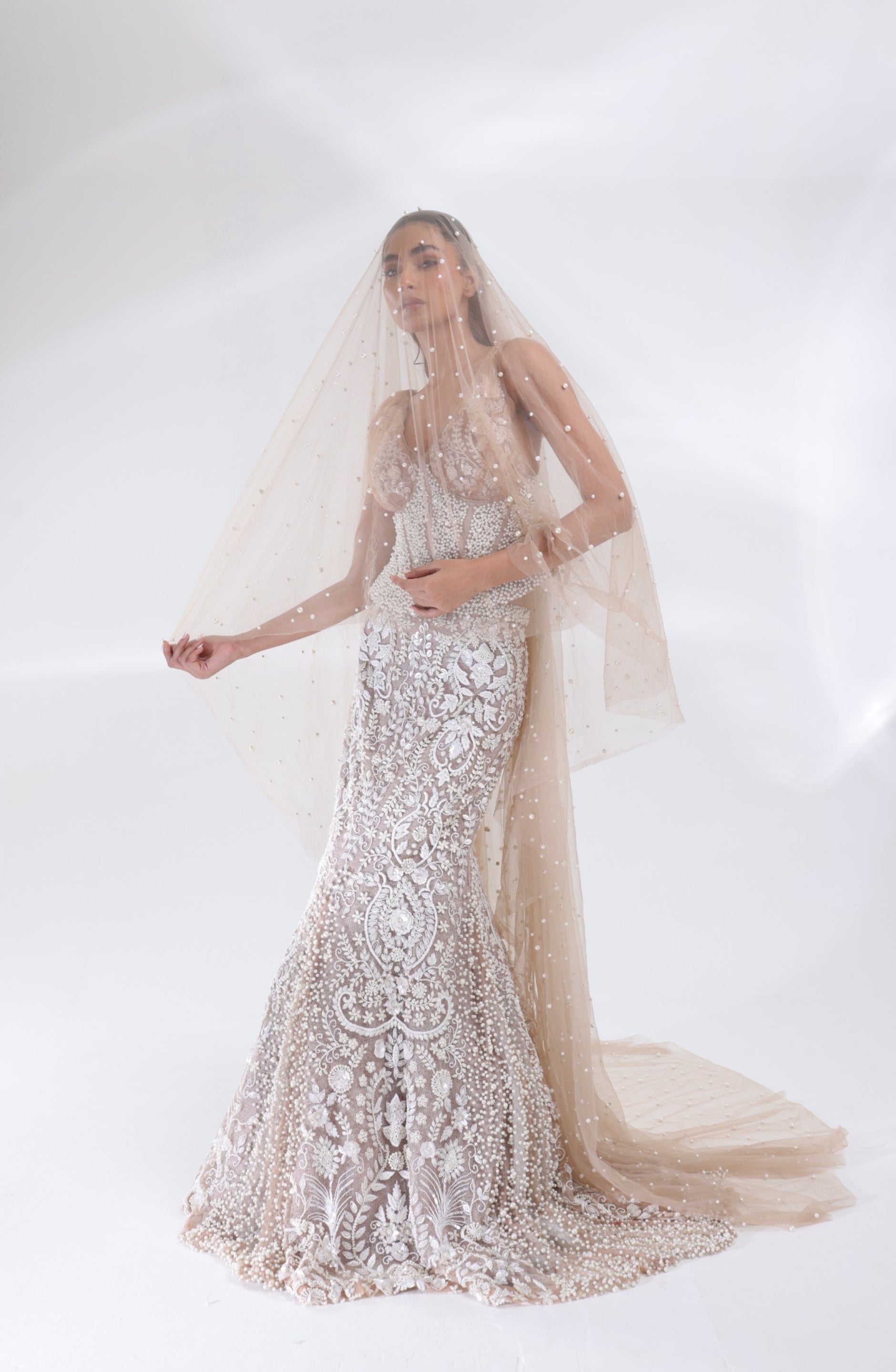 Champagne ivory Aurelia Pearl Mermaid Lehenga with a sheer pearl-embellished bridal veil draped over the model, highlighting the embroidered corset blouse and fitted mermaid silhouette by DEEPANSHI MASSEY LABEL.