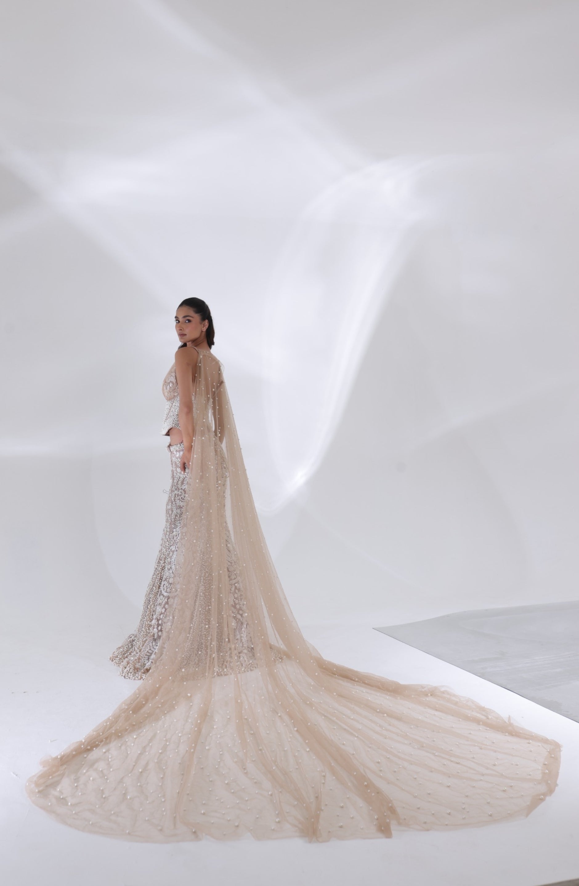 Champagne ivory Aurelia Pearl Mermaid Lehenga styled with a long pearl-detailed net veil and an intricately embroidered mermaid skirt, showcasing the ensemble's elegant bridal craftsmanship by DEEPANSHI MASSEY LABEL.