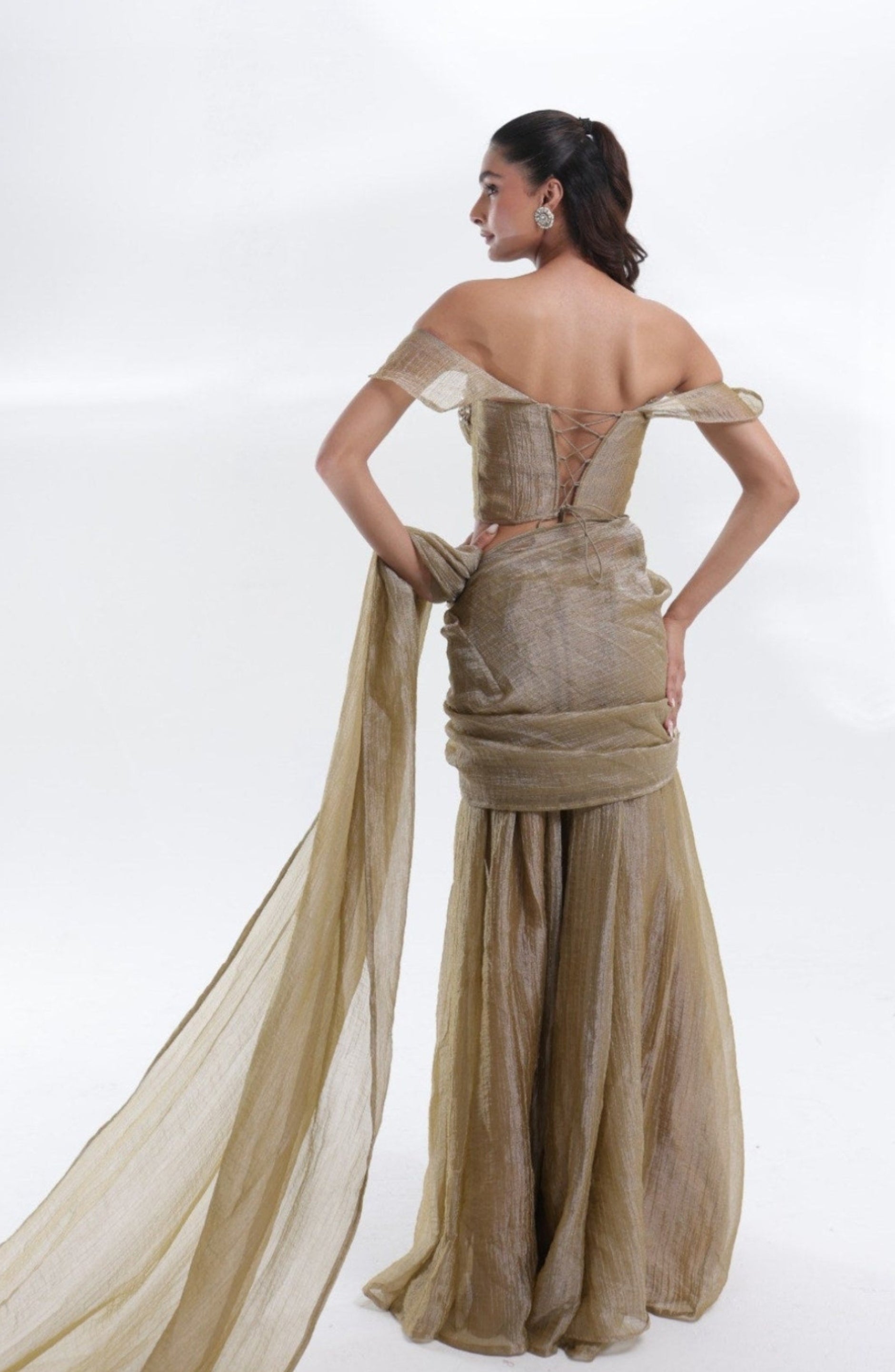 Back view of the Aurum Tissue Silk Saree by DEEPANSHI MASSEY LABEL showcasing the corset blouse with lace-up detailing, off-shoulder sleeves and a flowing champagne-gold tissue silk pallu.