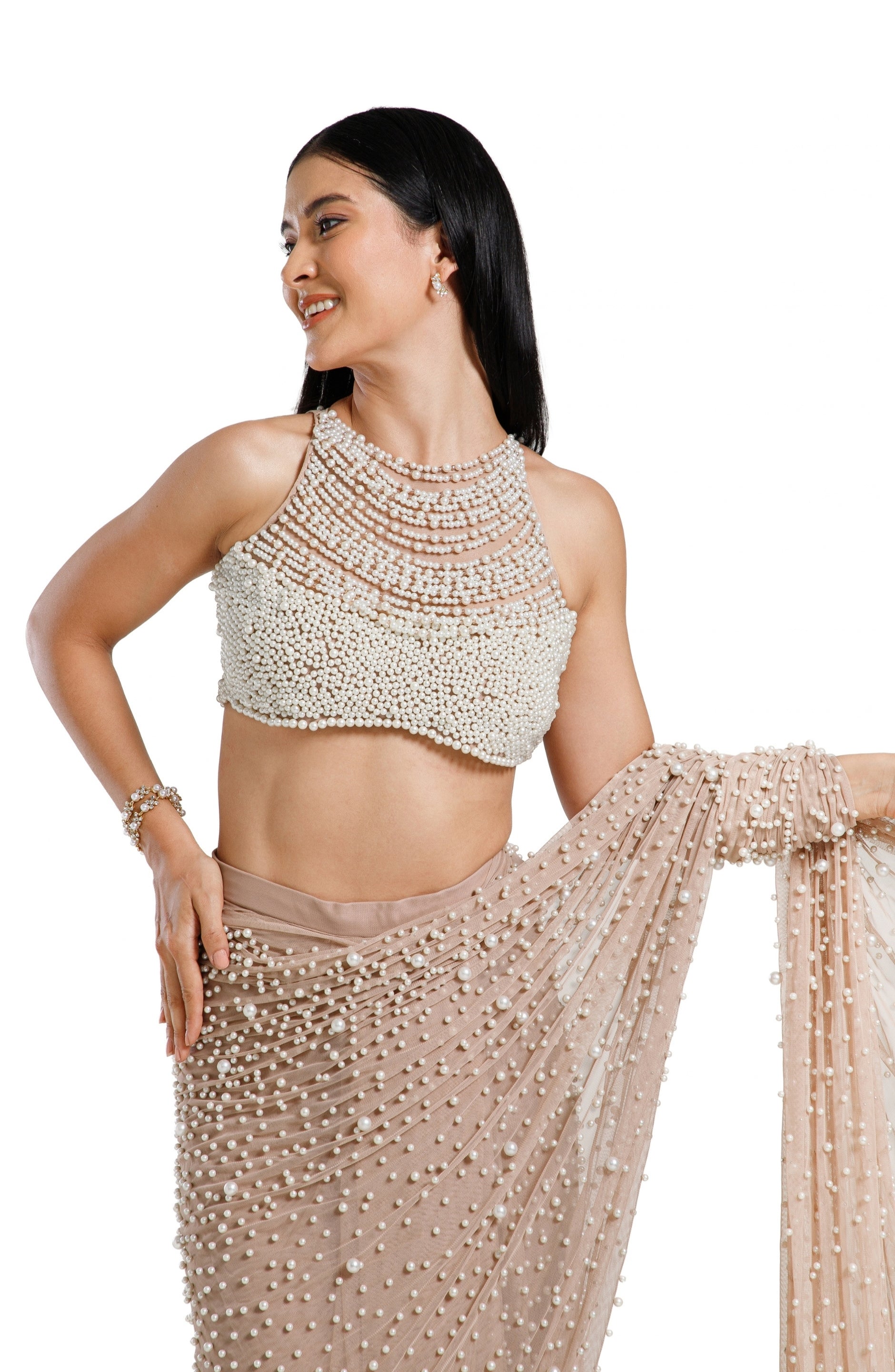Model wearing a champagne blush net saree hand-embellished with hundreds of cascading white pearls, paired with a matching concentric pearl halter blouse.