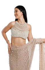 Model wearing a champagne blush net saree hand-embellished with hundreds of cascading white pearls, paired with a matching concentric pearl halter blouse.