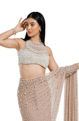 Model wearing a champagne blush net saree hand-embellished with hundreds of cascading white pearls, paired with a matching concentric pearl halter blouse.