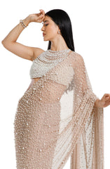 Model wearing a champagne blush net saree hand-embellished with hundreds of cascading white pearls, paired with a matching concentric pearl halter blouse.