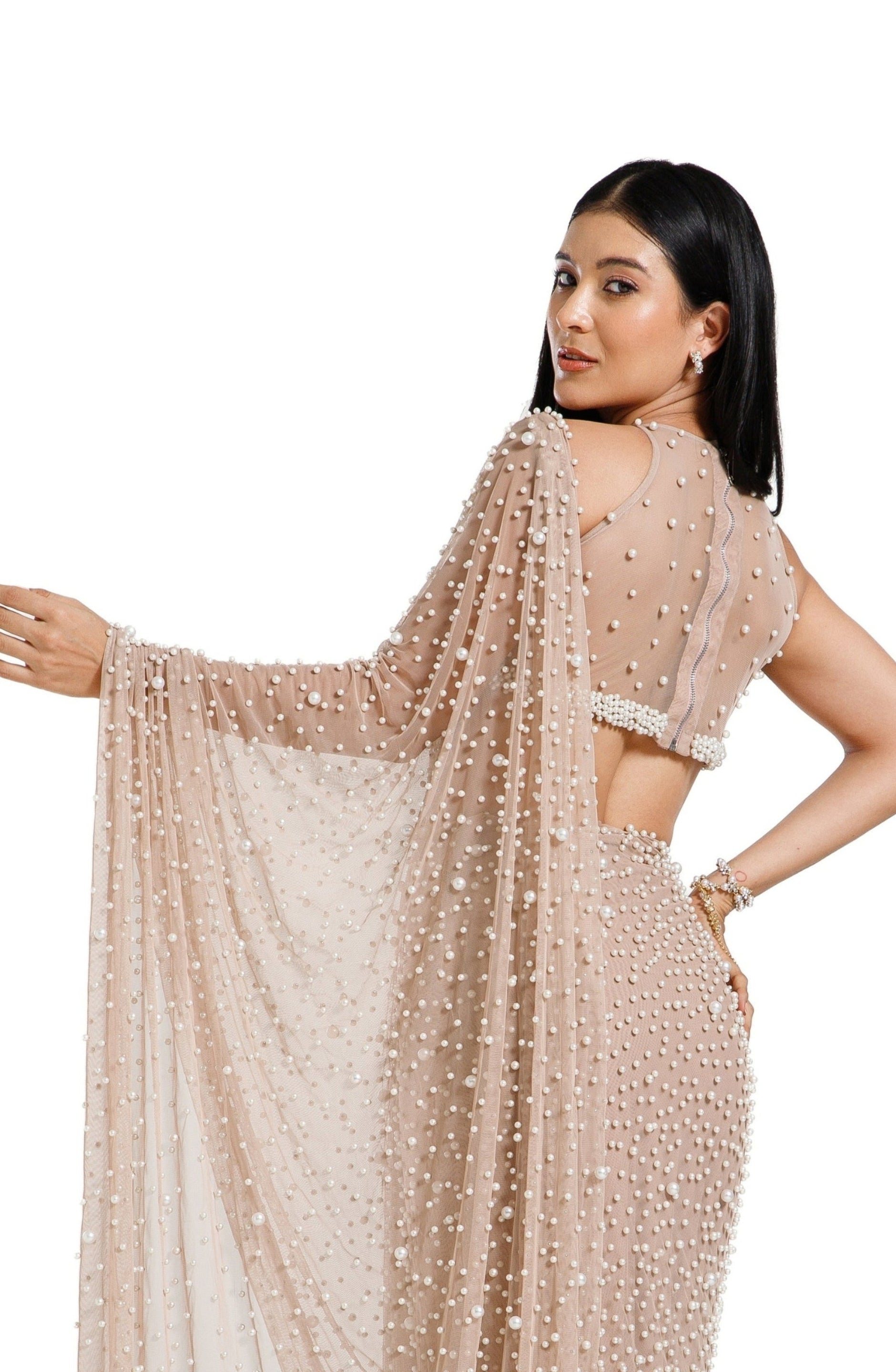 Model wearing a champagne blush net saree hand-embellished with hundreds of cascading white pearls, paired with a matching concentric pearl halter blouse.