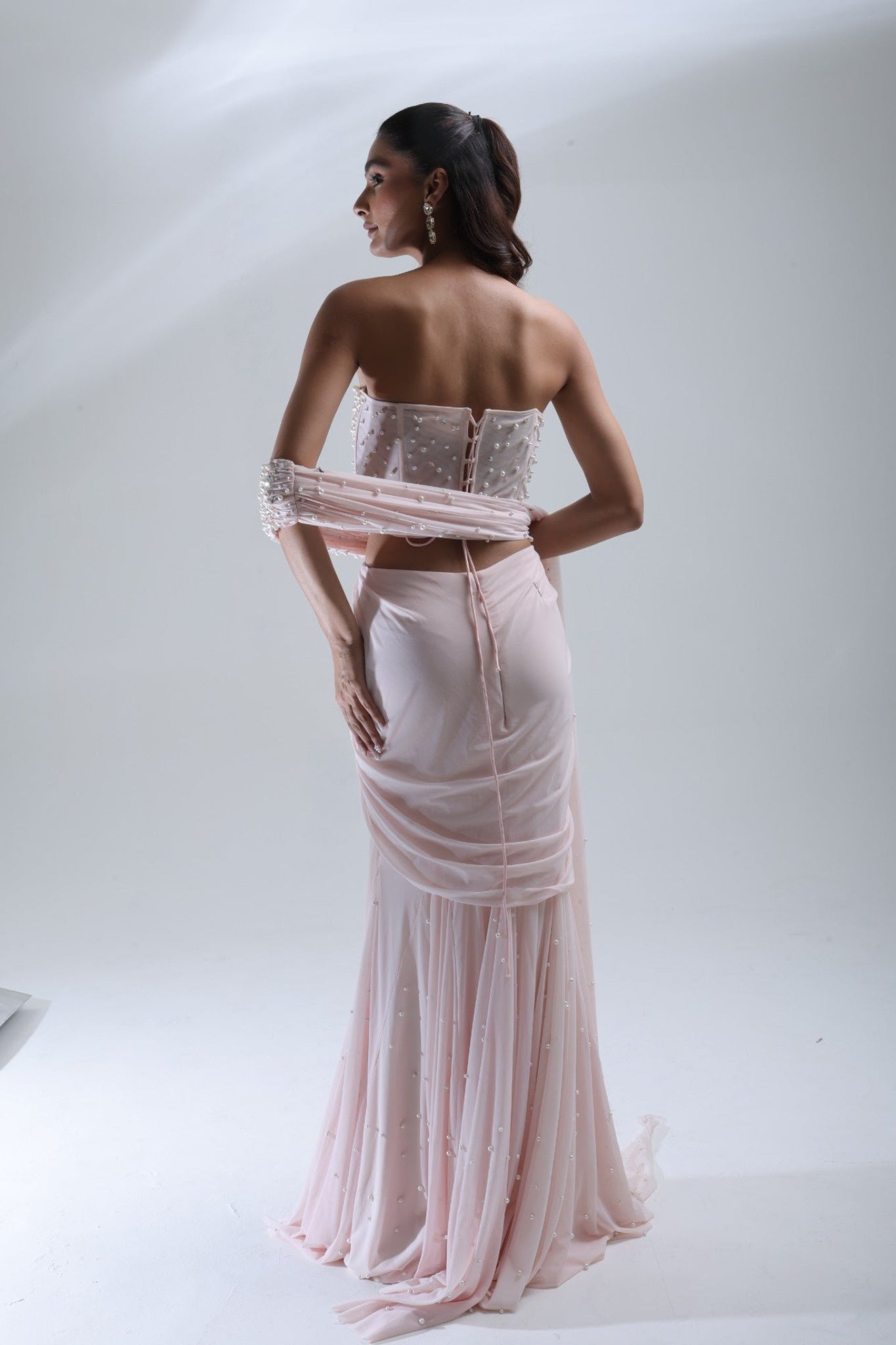 DEEPANSHI MASSEY LABEL back view of baby pink saree lehenga showing the blouse fastening, draped sleeve detail and skirt