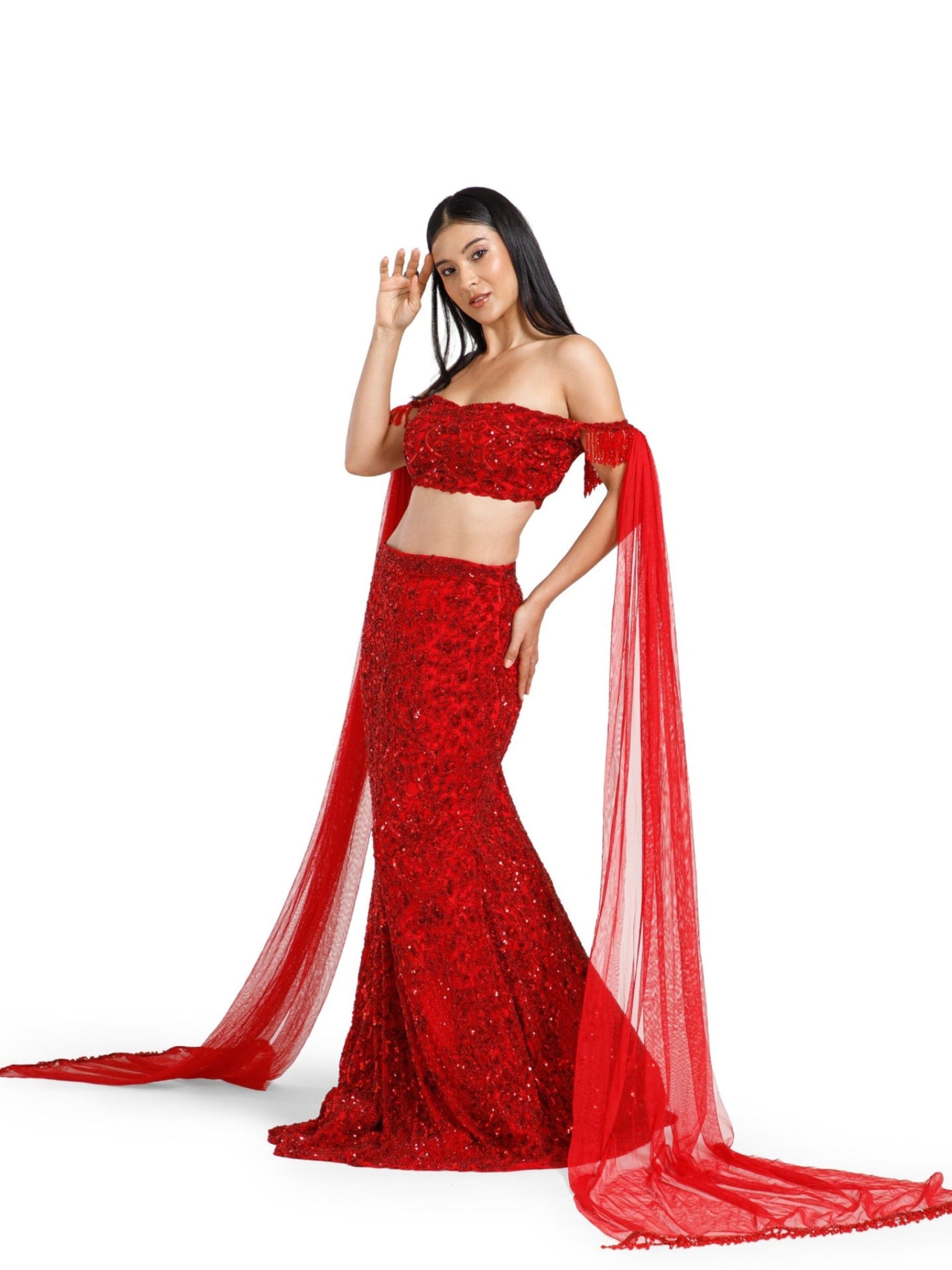 Crimson Reign Lehenga by DEEPANSHI MASSEY LABEL showcasing a fitted mermaid silhouette, embellished off-shoulder blouse and long flowing red net trail sleeves with handcrafted detailing.
