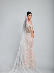 Side view of the beige fish cut lehenga by DEEPANSHI MASSEY LABEL, showcasing a sheer pearl-embellished cape draped over the embroidered blouse and skirt.