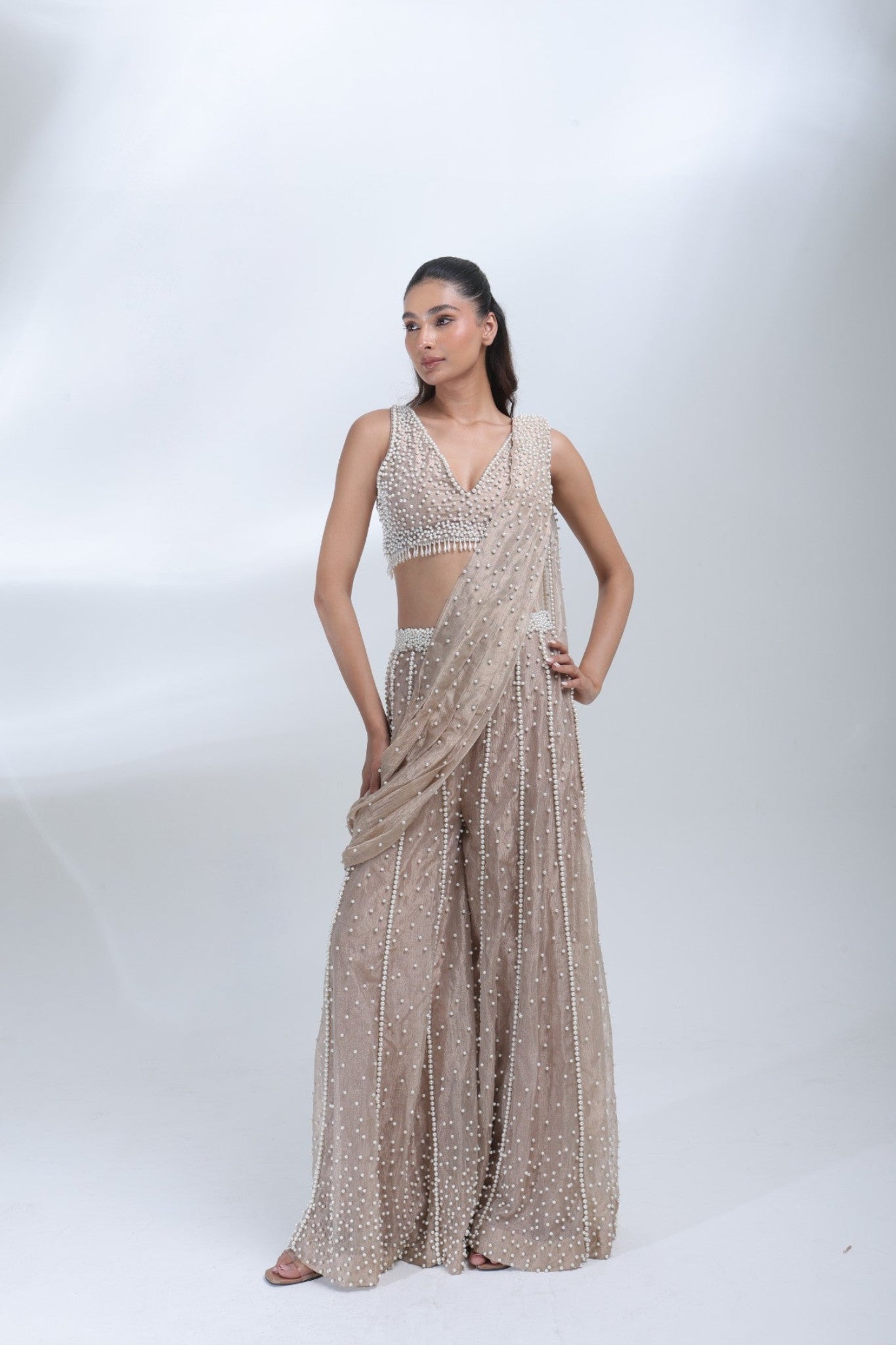 Opaline Sharara by DEEPANSHI MASSEY LABEL featuring a champagne beige tissue ensemble with intricate pearl embellishments, sleeveless V-neck blouse and flowing sharara pants.