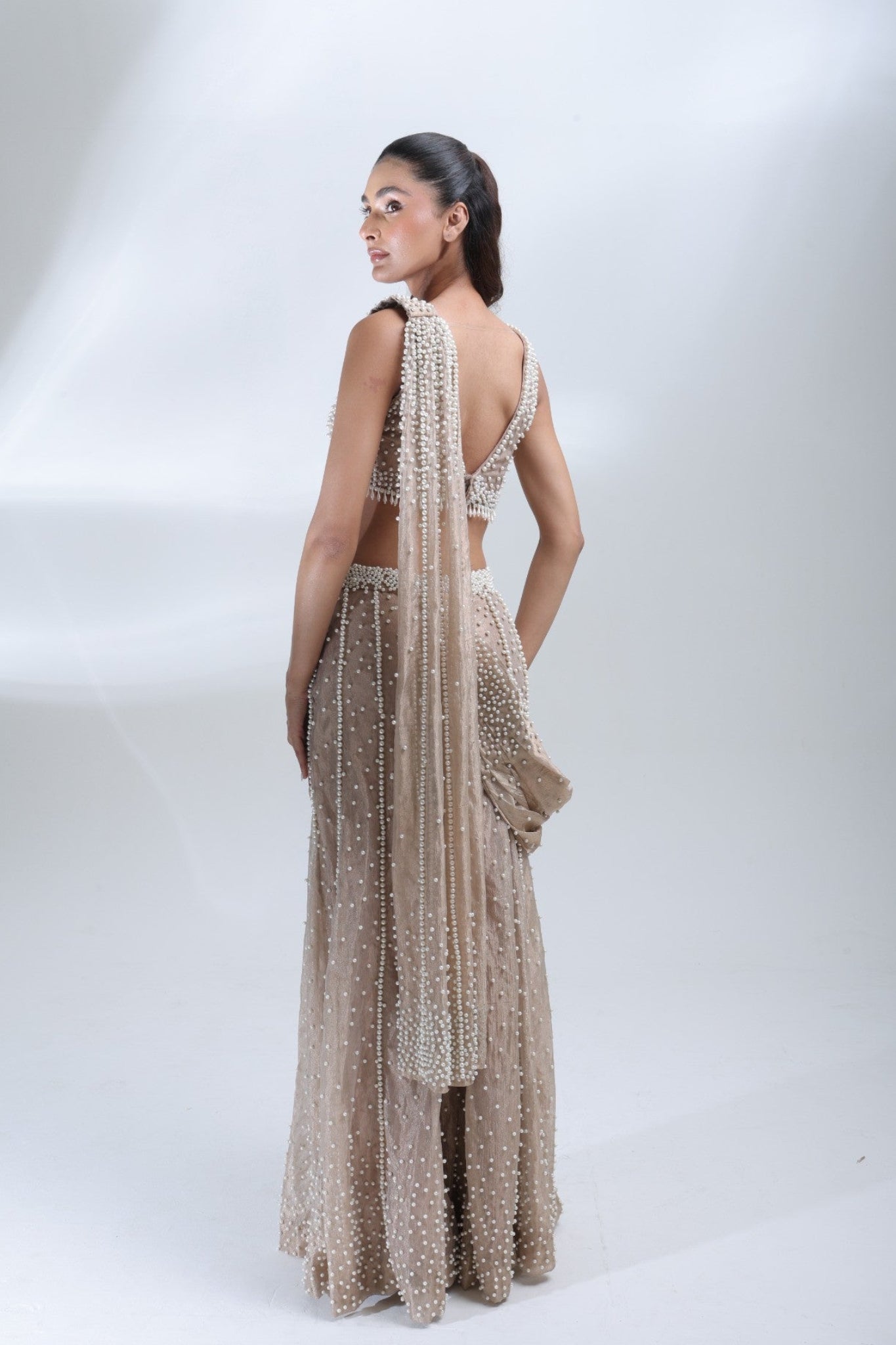 Back view of the Opaline Sharara by DEEPANSHI MASSEY LABEL showing the open-back blouse design, pearl embellishments and flowing champagne tissue dupatta.