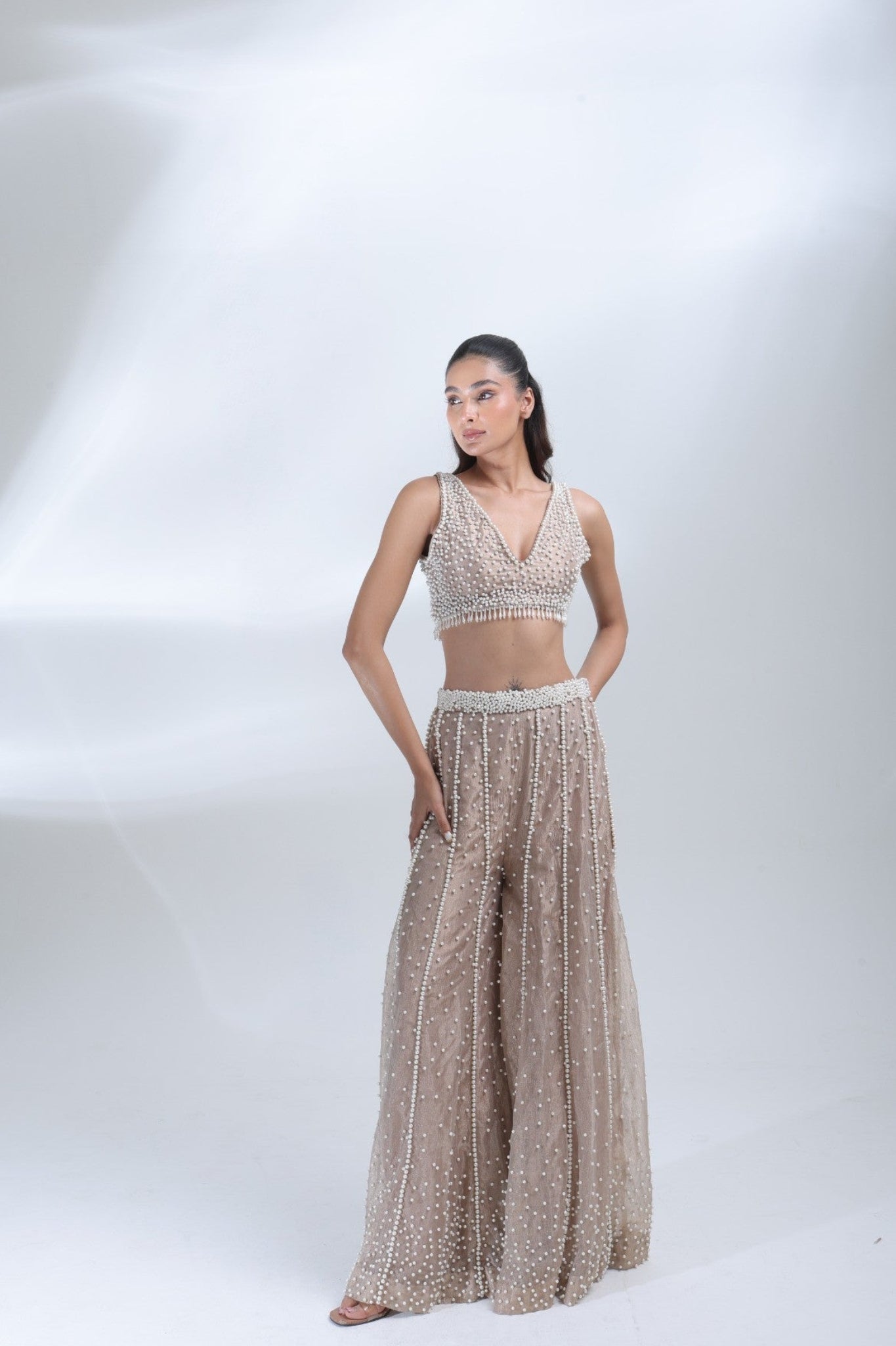 Opaline Sharara by DEEPANSHI MASSEY LABEL featuring a heavily pearl-embellished sleeveless blouse and matching champagne tissue sharara pants with intricate vertical pearl detailing.