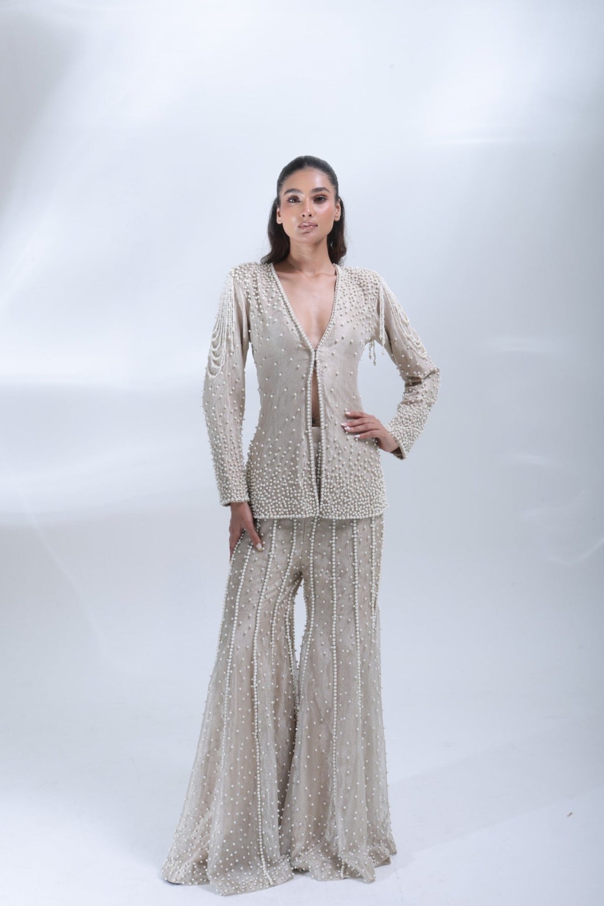 Full-length front view of a model wearing a champagne beige pearl-embellished jacket and matching wide-leg trousers.