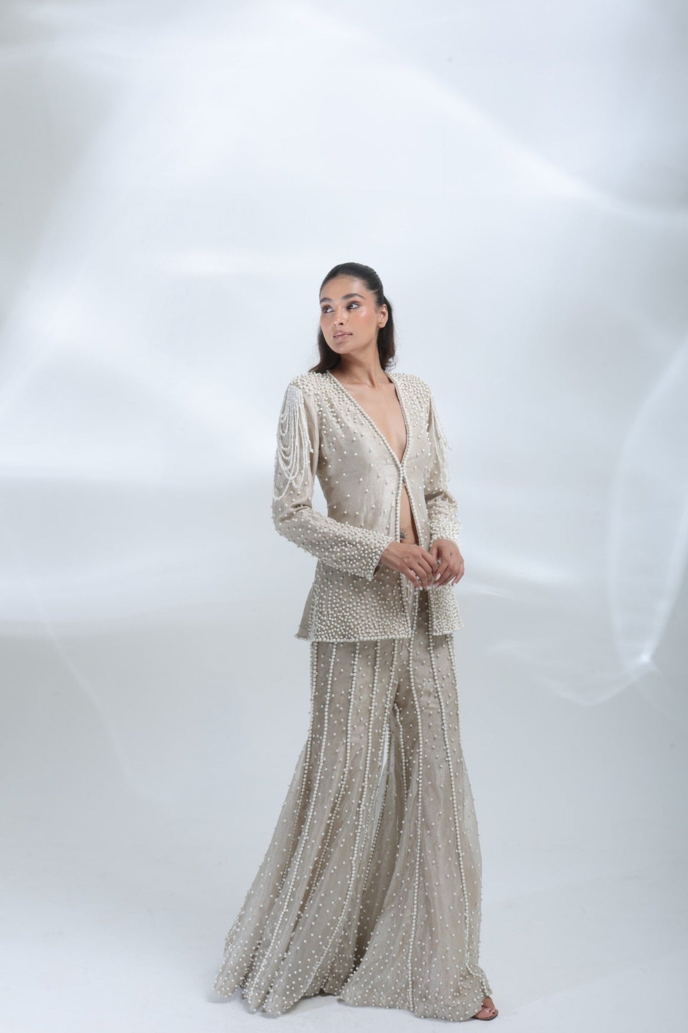 Three-quarter pose showcasing the pearl detailing and elegant silhouette of the champagne jacket and trouser set.