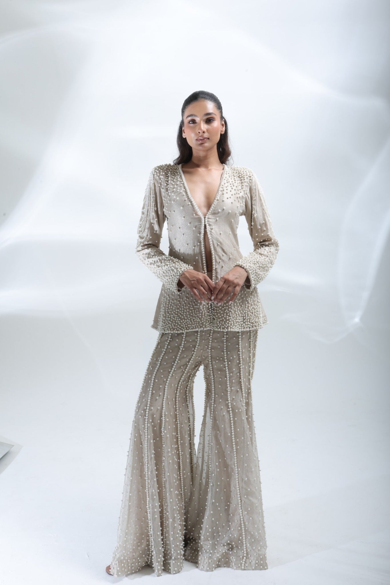 Front view of the model wearing a champagne pearl jacket with matching embellished trousers.