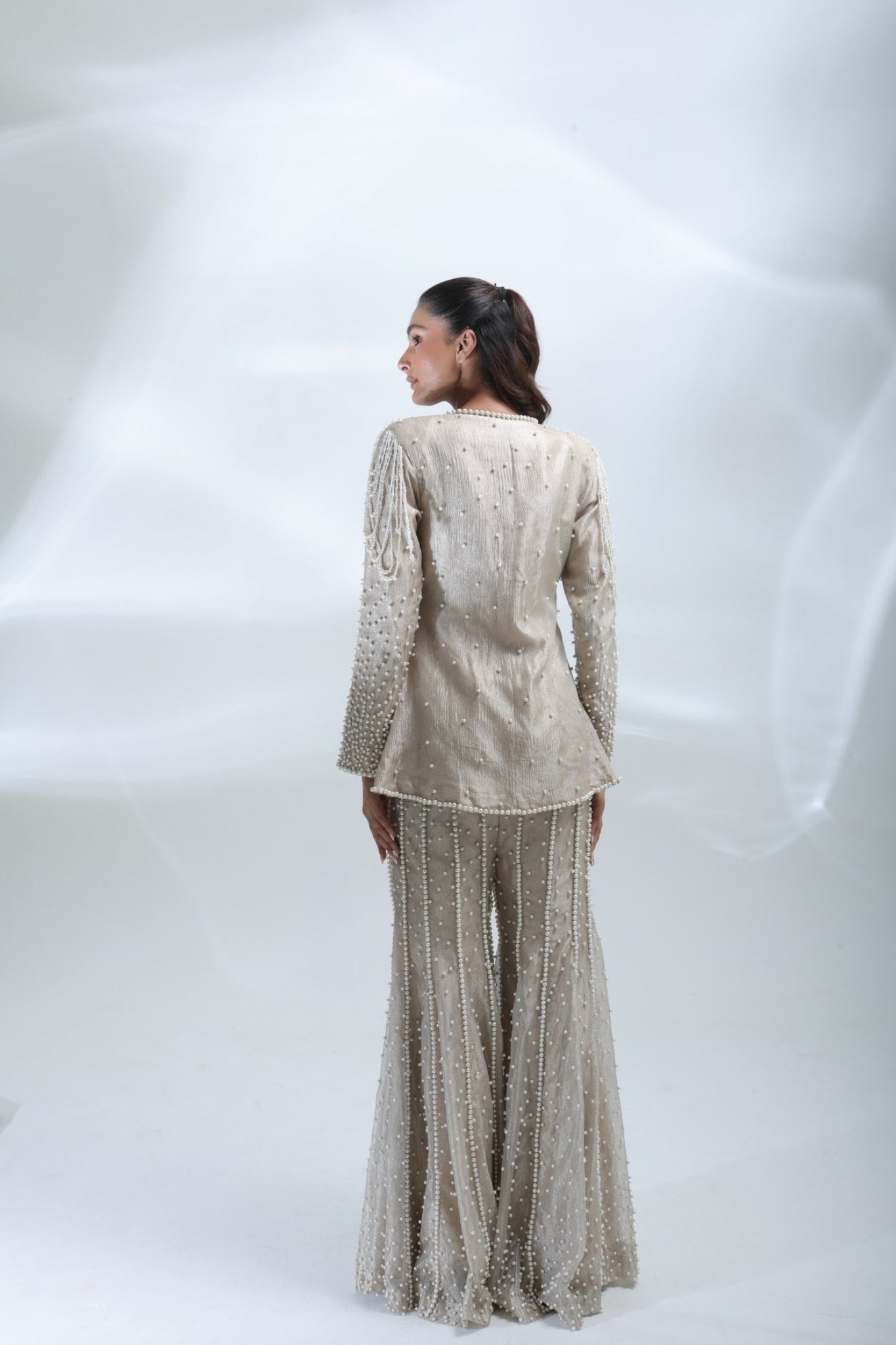Rear full-length view of the champagne pearl jacket and matching wide-leg trousers with vertical pearl detailing.