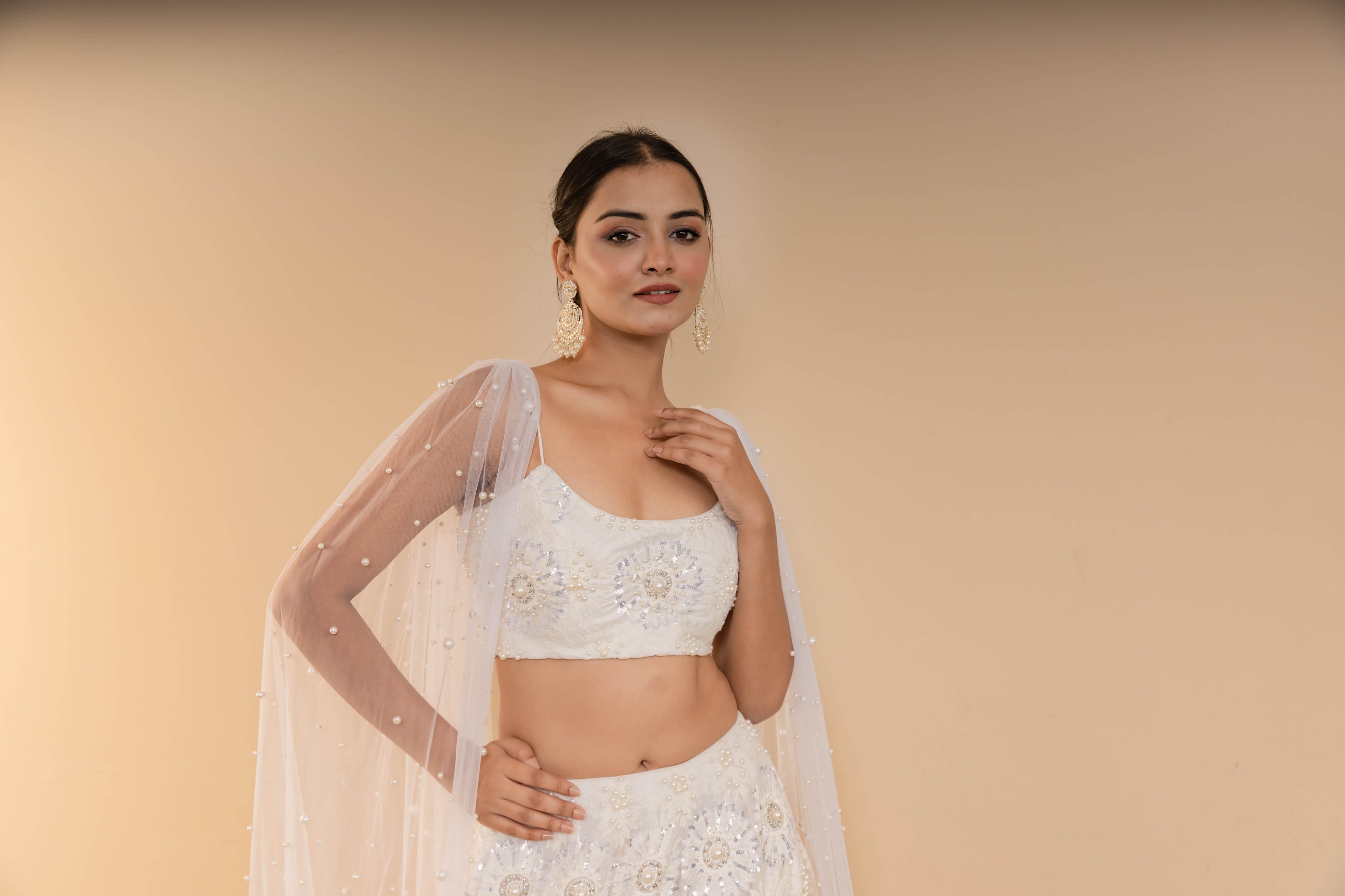 Woman wearing a white traditional outfit with a sheer dupatta against a beige background